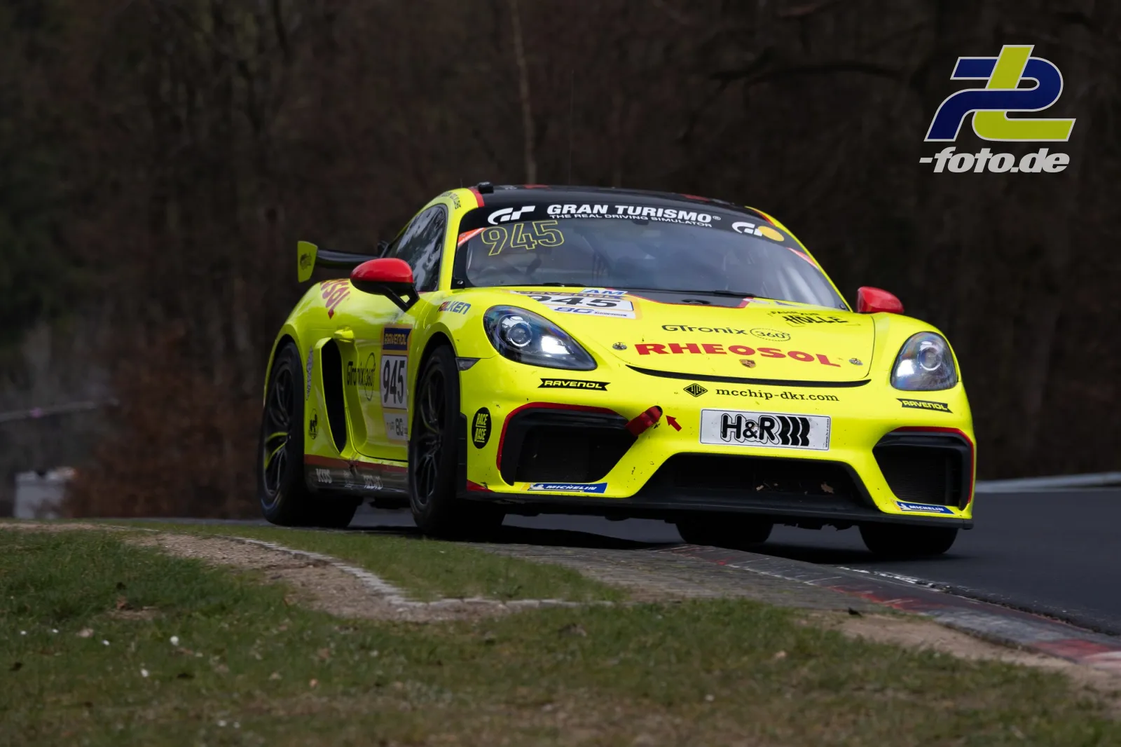 Gelber Porsche 718 Cayman GT4 Nr. 945 in Kurve auf der Nordschleife beim NLS-Rennen am Nürburgring.