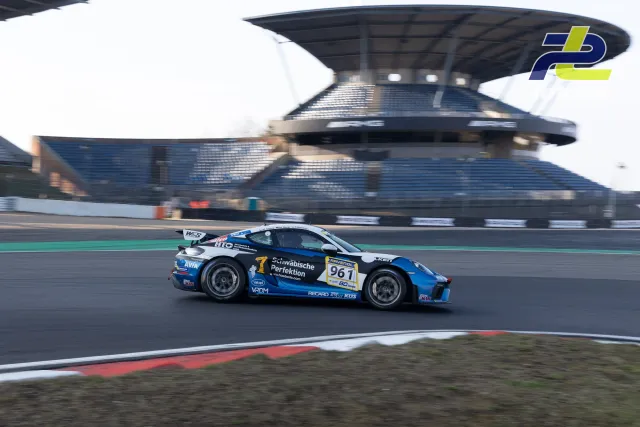 Porsche Cayman GT4 #961 in blau-schwarzer Lackierung fährt im Zeittraining auf dem Nürburgring, Tribüne im Hintergrund.