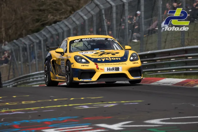 Gelber Porsche 718 Cayman GT4 Clubsport #953 mit cyclon-Lackierung in Kurve auf der Nürburgring-Nordschleife beim NLS-Rennen.