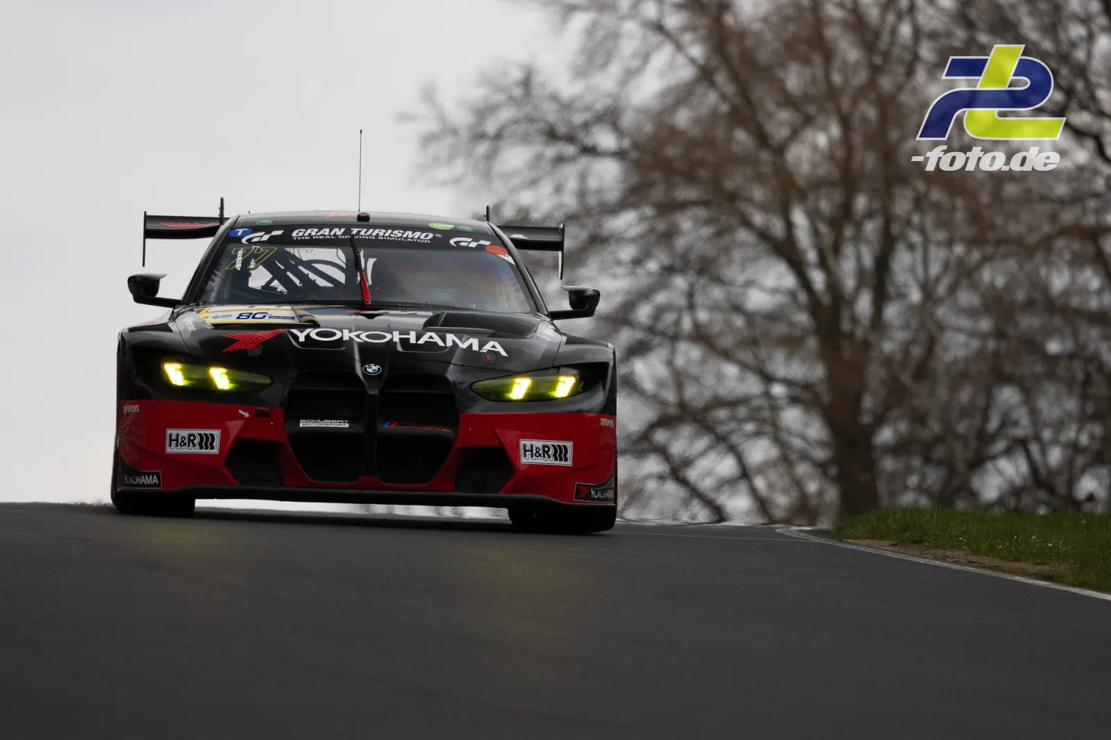 BMW M4 GT3 mit Yokohama-Lackierung in Kurve auf der Nordschleife bei trübem Wetter, Gran Turismo Schriftzug am Windschutzscheibenband.