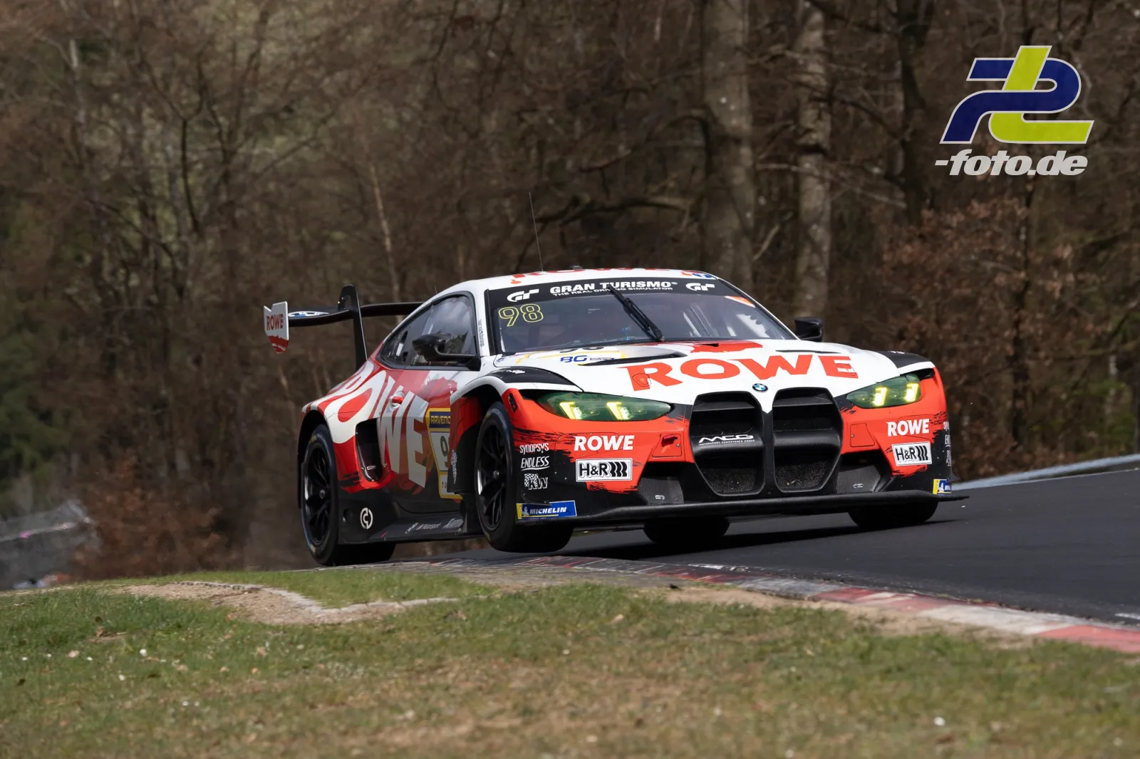 BMW M4 GT3 mit ROWE-Lackierung in Kurve auf der Nürburgring-Nordschleife, umgeben von kahlen Bäumen.