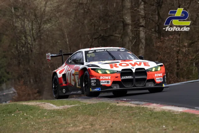 BMW M4 GT3 mit ROWE-Lackierung in Kurve auf der Nürburgring-Nordschleife, umgeben von kahlen Bäumen.