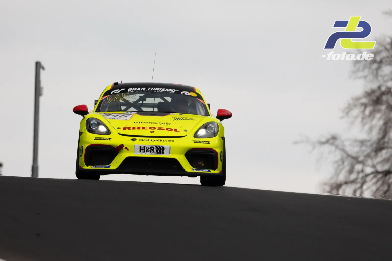 Gelber Porsche Cayman GT4 in Kuppe auf dem Nürburgring während NLS Rennen, frontale Ansicht mit Gran Turismo-Beklebung