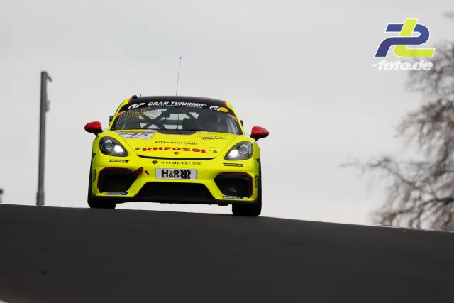 Gelber Porsche Cayman GT4 in Kuppe auf dem Nürburgring während NLS Rennen, frontale Ansicht mit Gran Turismo-Beklebung
