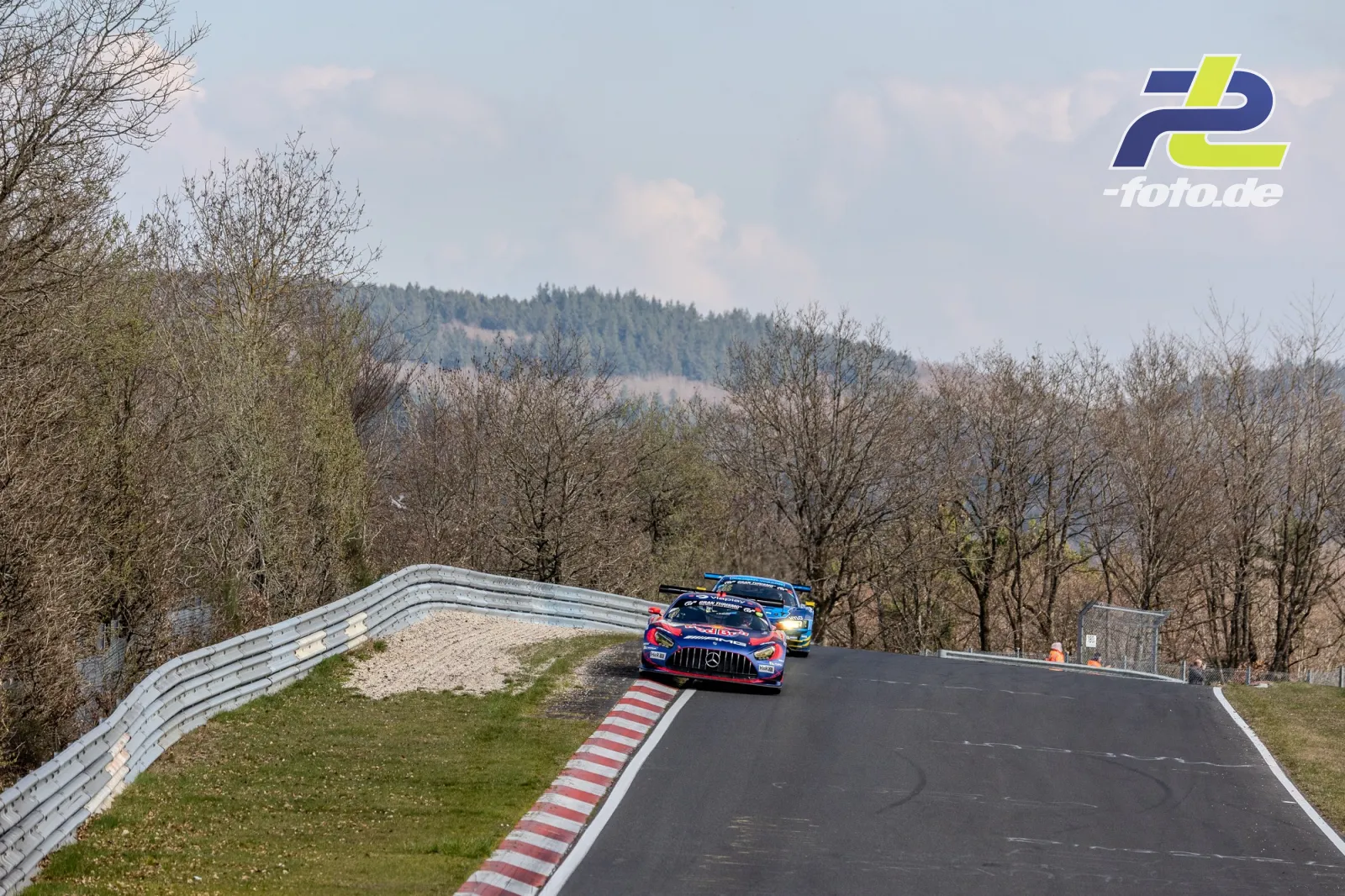 Zwei GT3-Rennwagen auf der Nordschleife bei einem Überholmanöver in einer Kurve, hügelige Eifellandschaft im Hintergrund.