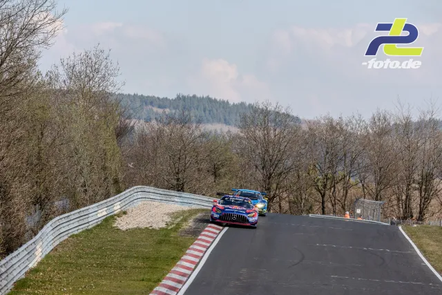 Zwei GT3-Rennwagen auf der Nordschleife bei einem Überholmanöver in einer Kurve, hügelige Eifellandschaft im Hintergrund.