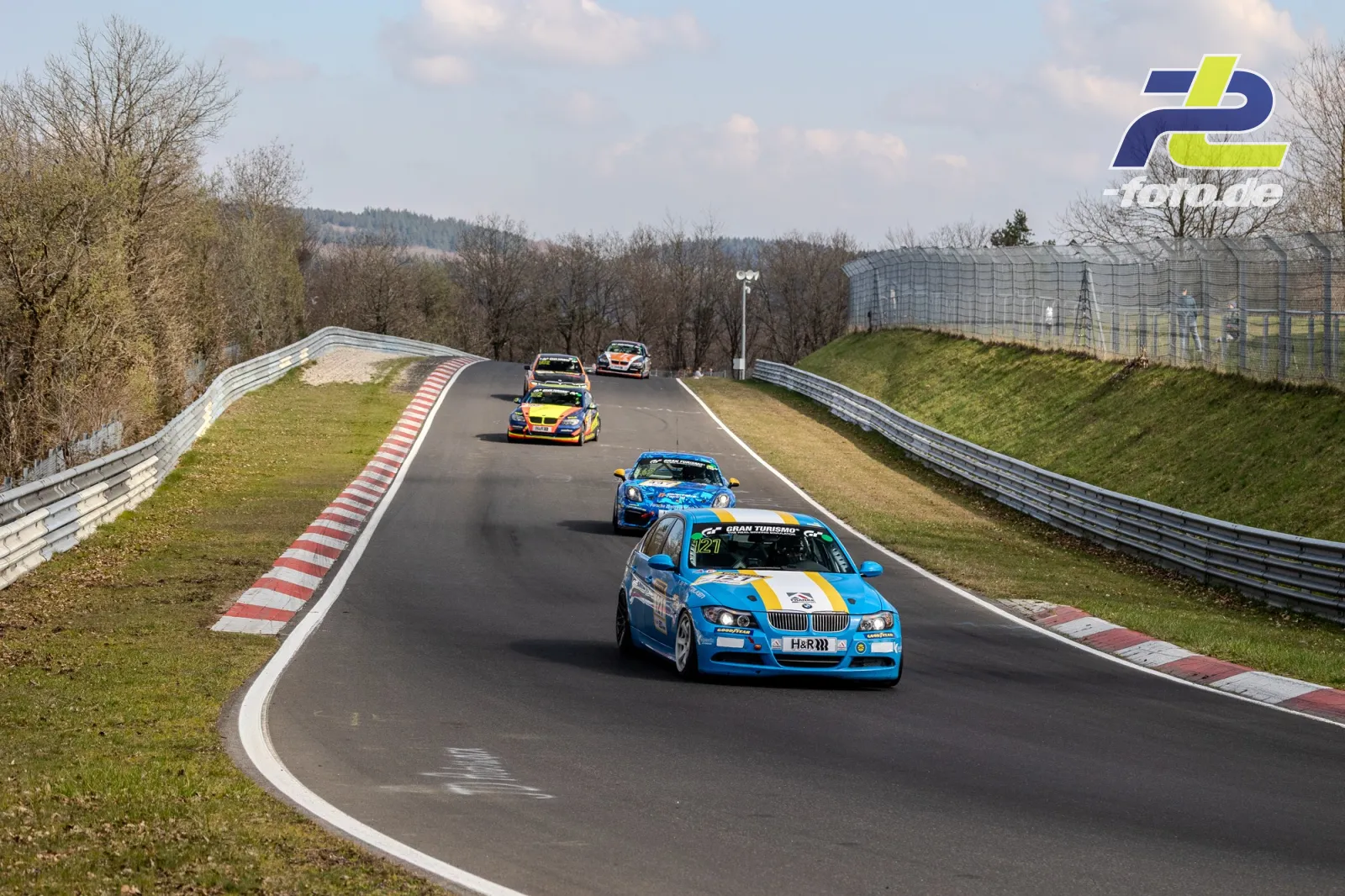 Sechs Rennwagen in Kolonne auf der Nordschleife des Nürburgrings während des NLS-Rennens, blaues BMW-Fahrzeug führt das Feld an.