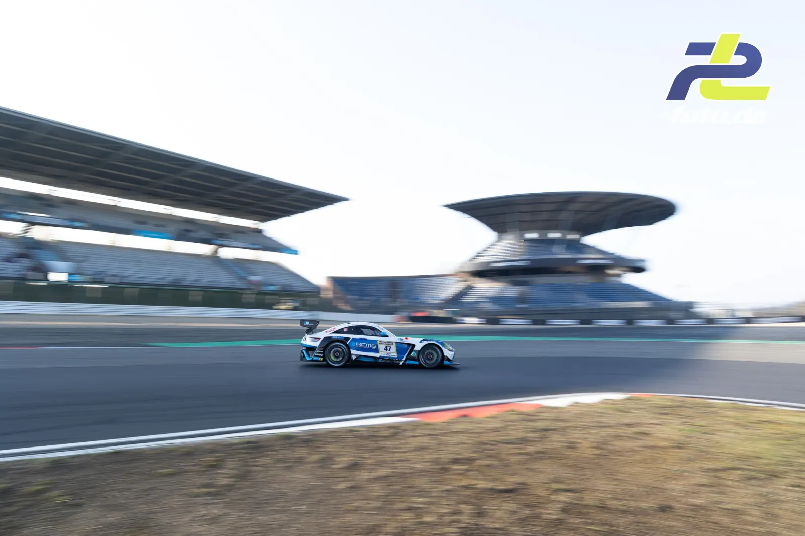 Rennsportwagen mit weißer und blauer Lackierung bei Zeittraining auf der Nürburgring-Nordschleife, Pagode im Hintergrund.