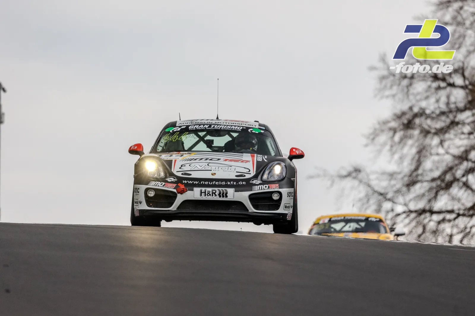 Porsche Cayman über eine Kuppe fahrend bei grauem Himmel und winterlichen Bedingungen mit verschneiten Bäumen am Nürburgring.