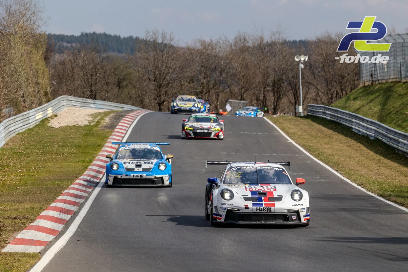 GT3-Fahrzeuge im Rennverkehr auf der Nordschleife, Porsche führt vor blauem Verfolger und weiteren Konkurrenten.