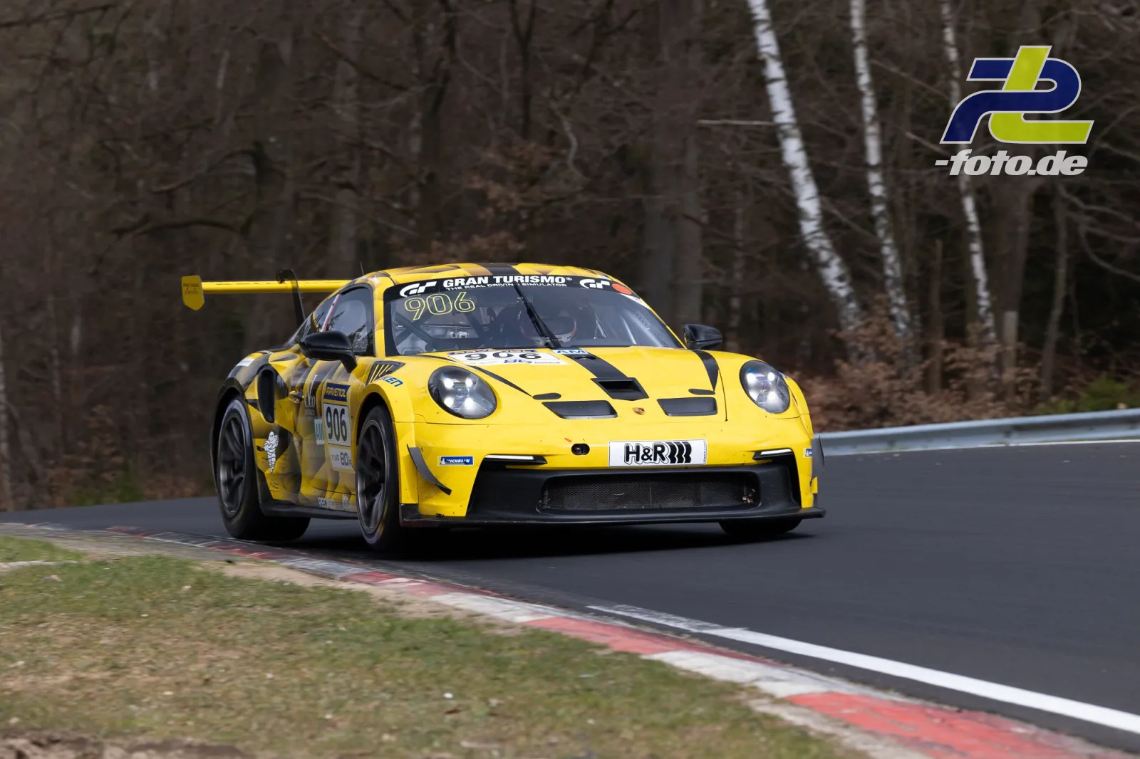 Gelber Porsche 911 GT3 R #906 in einer Kurve auf der Nürburgring-Nordschleife beim NLS-Rennen.