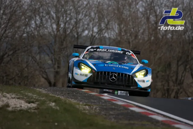 Mercedes-AMG GT3 in blau-weißer Lackierung in Kurve auf der Nordschleife, kahle Bäume im Hintergrund