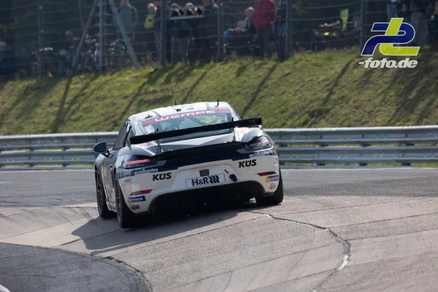 Porsche Cayman mit weißer KUS-Lackierung in der Kurve beim NLS-Rennen auf dem Nürburgring, Heckansicht
