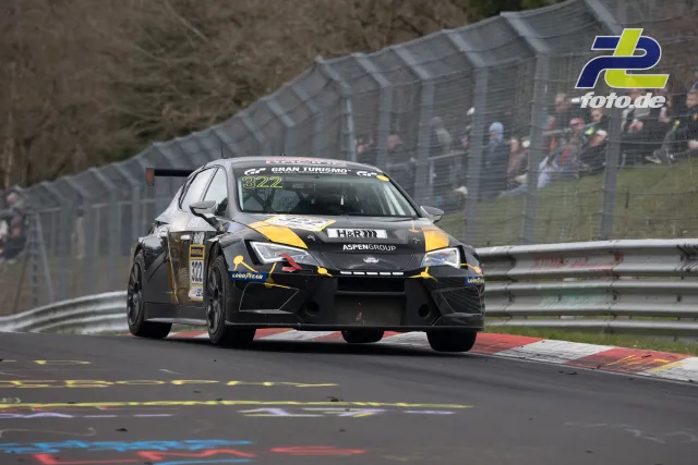 Audi TCR #322 des Aspen Group Teams in schwarz-gelber Lackierung auf der Nordschleife, Zuschauer im Hintergrund.