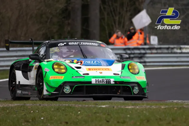 Porsche 911 GT3 R in grün-weißer Lackierung mit Startnummer 54 während des Rennens auf dem Nürburgring, Streckenposten im Hintergrund