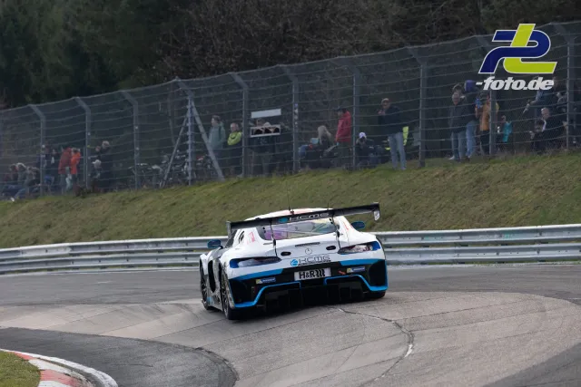 Mercedes-AMG GT3 in weiß-blauer Lackierung in Kurve auf der Nordschleife, Zuschauer am Zaun