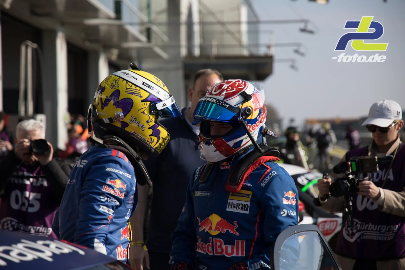 Zwei Red Bull Fahrer in Rennoveralls und Helmen nach dem Rennen in der Boxengasse am Nürburgring