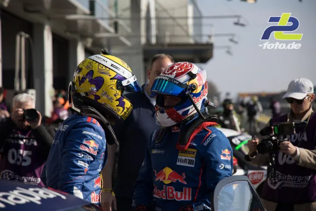 Zwei Red Bull Fahrer in Rennoveralls und Helmen nach dem Rennen in der Boxengasse am Nürburgring