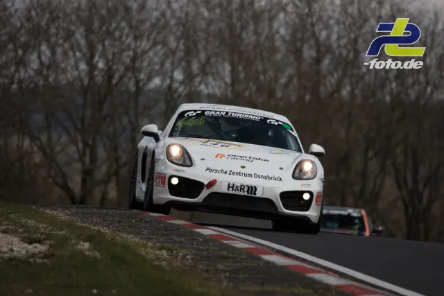 Weißer Porsche Cayman im Renntempo auf der Nordschleife mit kahlen Bäumen im Hintergrund, NLS Lauf 2