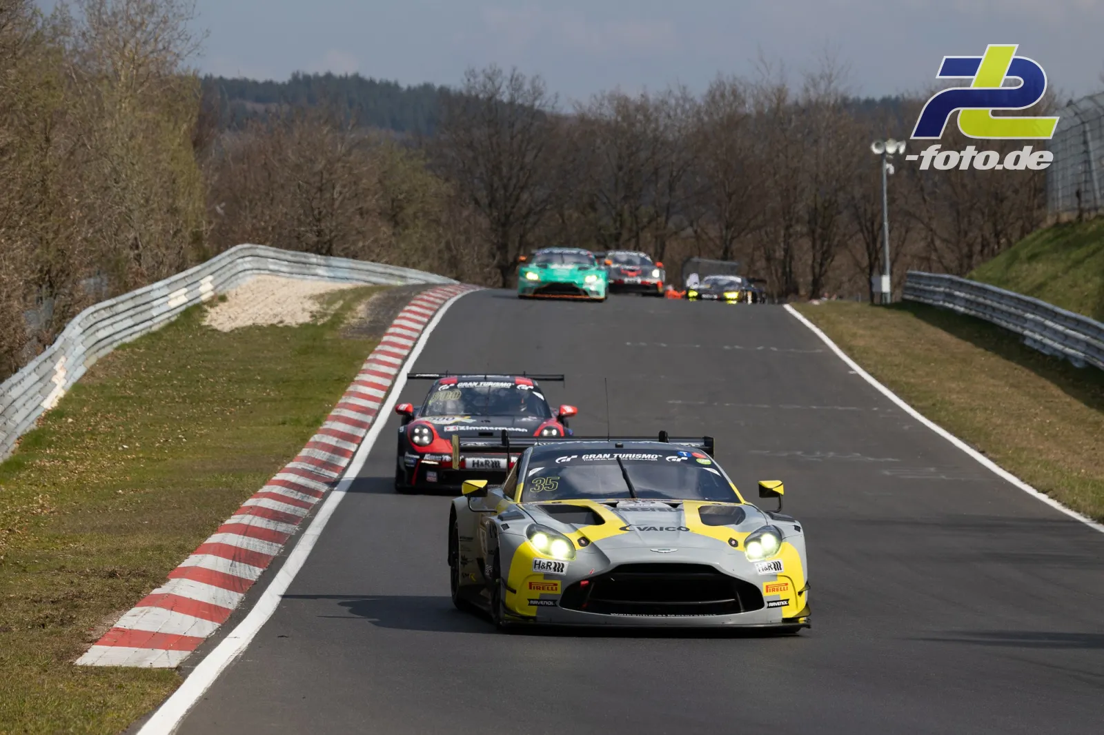 Mehrere GT-Fahrzeuge in einer Rechtskurve am Nürburgring während des 58. ADAC Barbarossapreis, angeführt von einem silber-gelben Aston Martin.