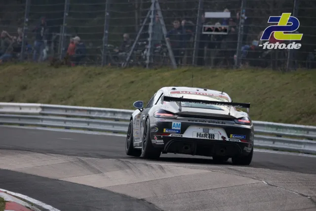 Weißer Porsche GT-Rennwagen von hinten in einer Kurve auf dem Nürburgring, Zuschauer hinter dem Fangzaun.