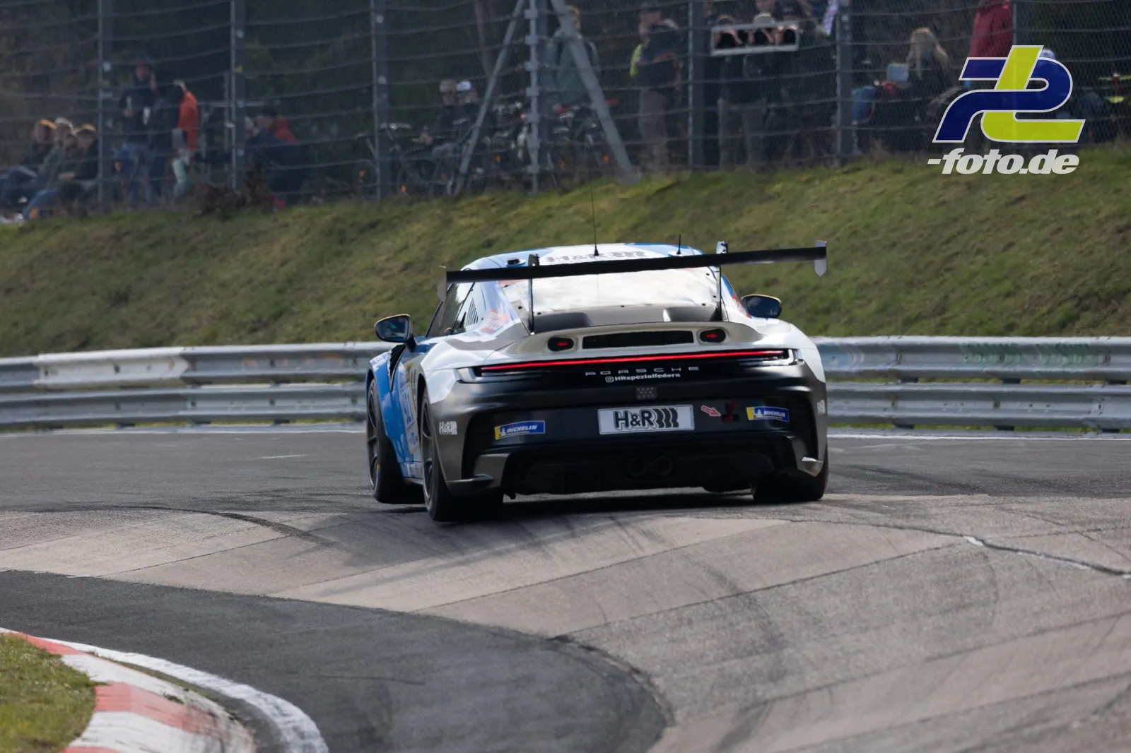Porsche 992 GT3 Cup in weiß-blauer Lackierung von hinten in Rechtskurve auf der Nordschleife beim NLS Rennen am Nürburgring.