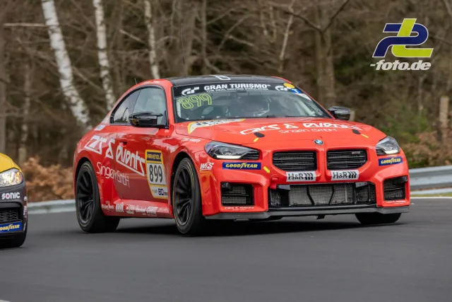 Orange-roter BMW M2 Nummer 899 auf der Nordschleife während des NLS-Rennens, waldgesäumte Strecke im Hintergrund.