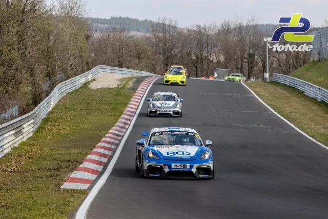 Vier Rennwagen in einer Rechtskurve auf der Nordschleife, angeführt von einem blauen Porsche Cayman GT4.