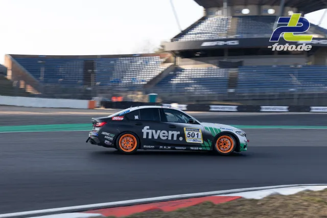 BMW Tourenwagen Nr. 501 mit Fiverr-Lackierung beim Zeittraining auf dem Nürburgring, Mitzieher mit Tribüne im Hintergrund.