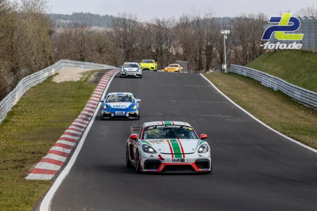 Mehrere Rennfahrzeuge im Rennen auf der Nordschleife des Nürburgrings bei bewölktem Himmel.