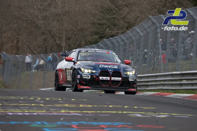 BMW M4 GT4 mit Coca-Cola-Lackierung auf der Nordschleife während des NLS-Rennens, Startnummer 130, im Flug über eine Kuppe.