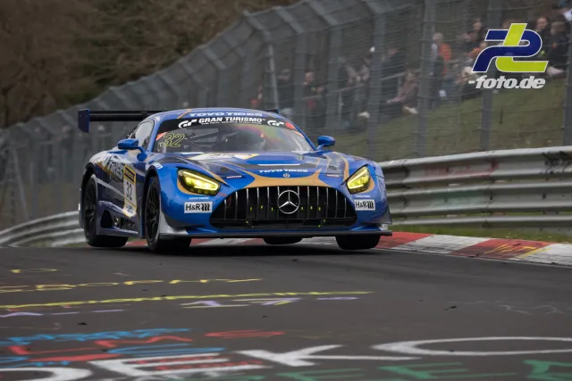 Mercedes-AMG GT3 #32 in Blau-Grau auf der Nürburgring-Nordschleife während des NLS-Rennens mit Zuschauern im Hintergrund.