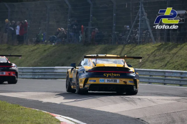 Gelb-schwarzer Porsche 911 GT3 R mit cyclon-Sponsoring in Kurve auf dem Nürburgring, Zuschauer im Hintergrund.