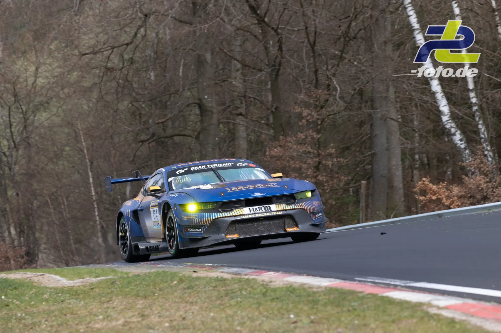 Ford Mustang GT3 #64 in blauer Lackierung fährt durch bewaldete Kurve auf der Nürburgring-Nordschleife beim NLS-Rennen.