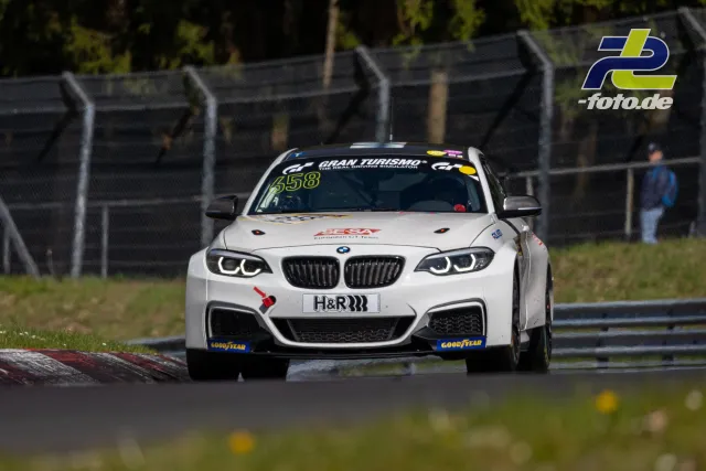 Weißer BMW M240i mit Startnummer 658 in Kurve auf dem Nürburgring während NLS-Rennen, Frontalansicht mit Randstein im Vordergrund.