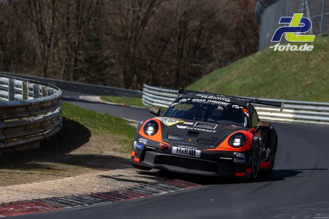 Porsche 911 GT3 Cup in schwarz-orange bei schneller Kurvenfahrt auf der Nordschleife, mit Heckspoiler und Renngrafik.