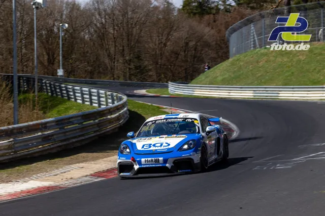 Rennwagen auf der Nordschleife in einer Kurve, vorne ein blau-weißer Porsche mit BGS-Sponsoring