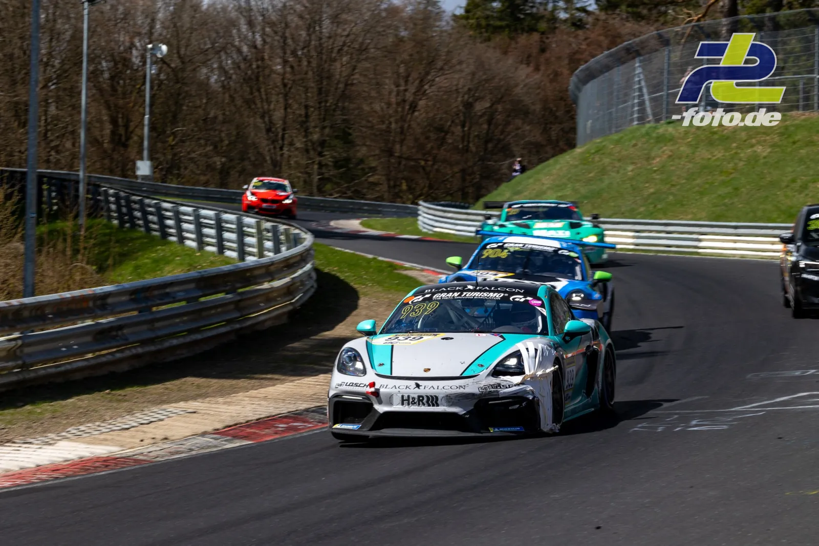 Porsche 718 Cayman GT4 mit türkis-weißer Lackierung führt eine Gruppe durch eine Kurve auf der Nordschleife