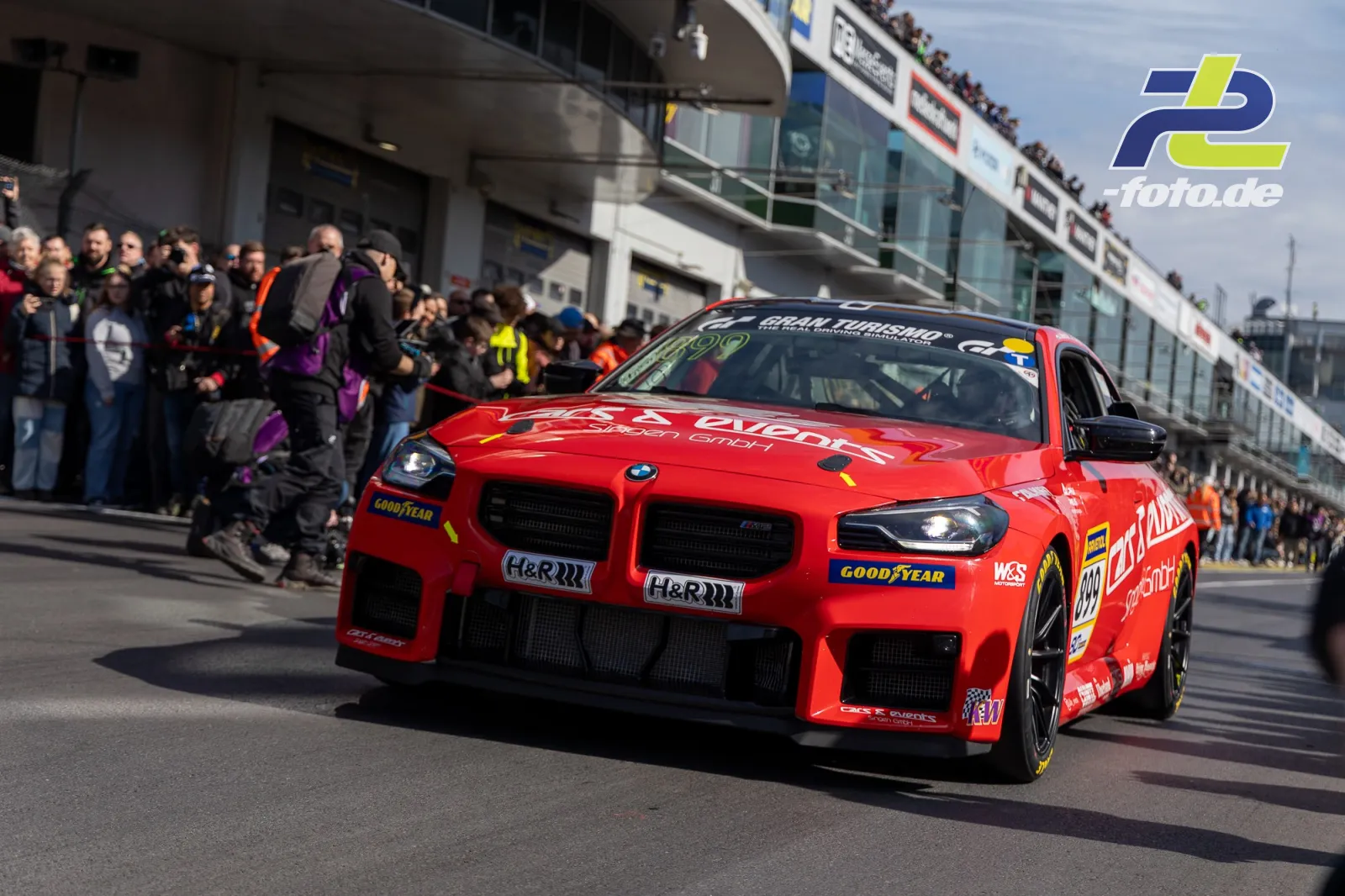 Roter BMW mit Startnummer 899 fährt durch die Boxengasse am Nürburgring, Zuschauer im Hintergrund.