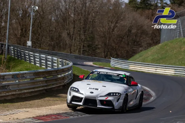 Toyota Supra in Kurve auf der Nordschleife mit Leitplanken und Randsteinen im Hintergrund.
