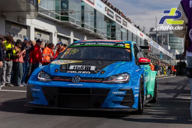 VW Golf GTI TCR mit blau-grüner Falken-Lackierung fährt durch die Boxengasse am Nürburgring, Zuschauer am Rand.