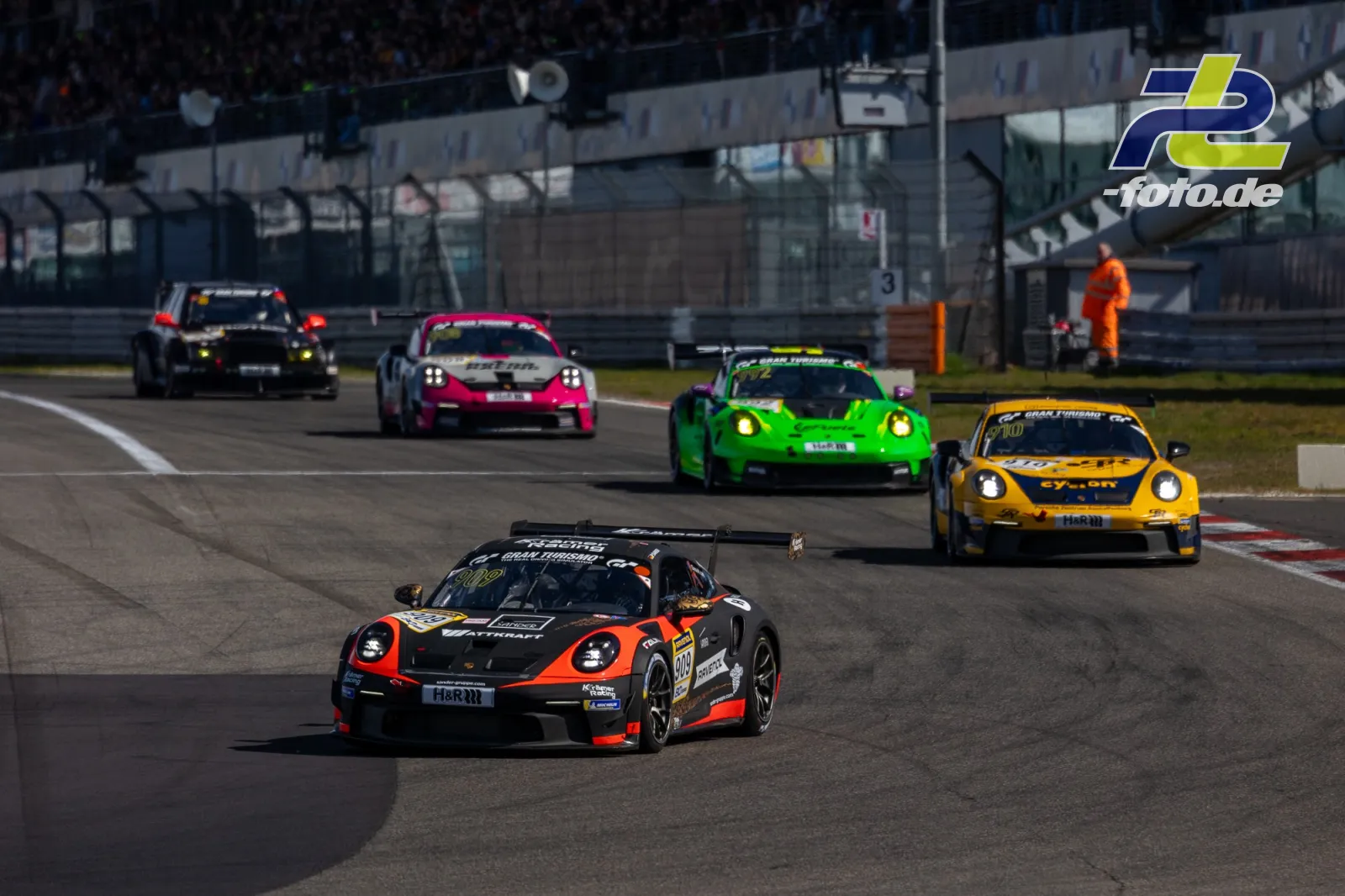 Fünf Rennwagen in einer Kurve auf der Nordschleife, angeführt von einem schwarz-orange lackierten Porsche 911 GT3 Cup.