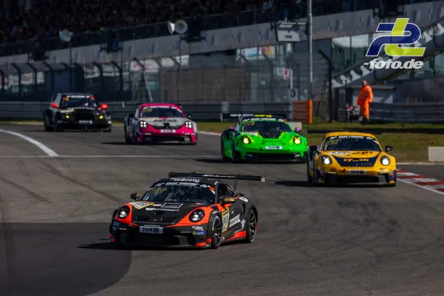 Fünf Rennwagen in einer Kurve auf der Nordschleife, angeführt von einem schwarz-orange lackierten Porsche 911 GT3 Cup.