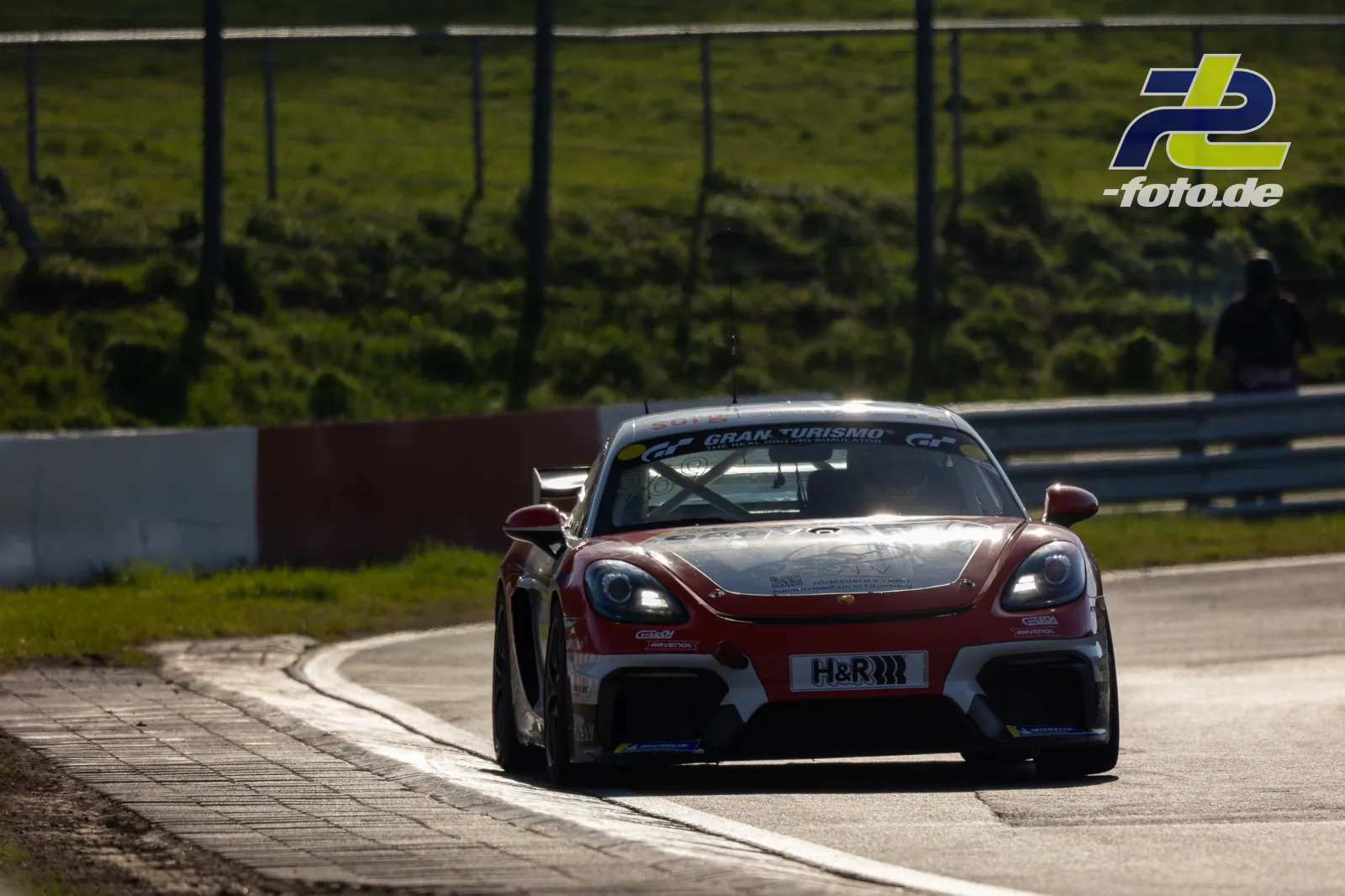 Weinrot-weißer Porsche 718 Cayman GT4 in Kurve auf dem Nürburgring beim NLS-Zeittraining, Frontalansicht.