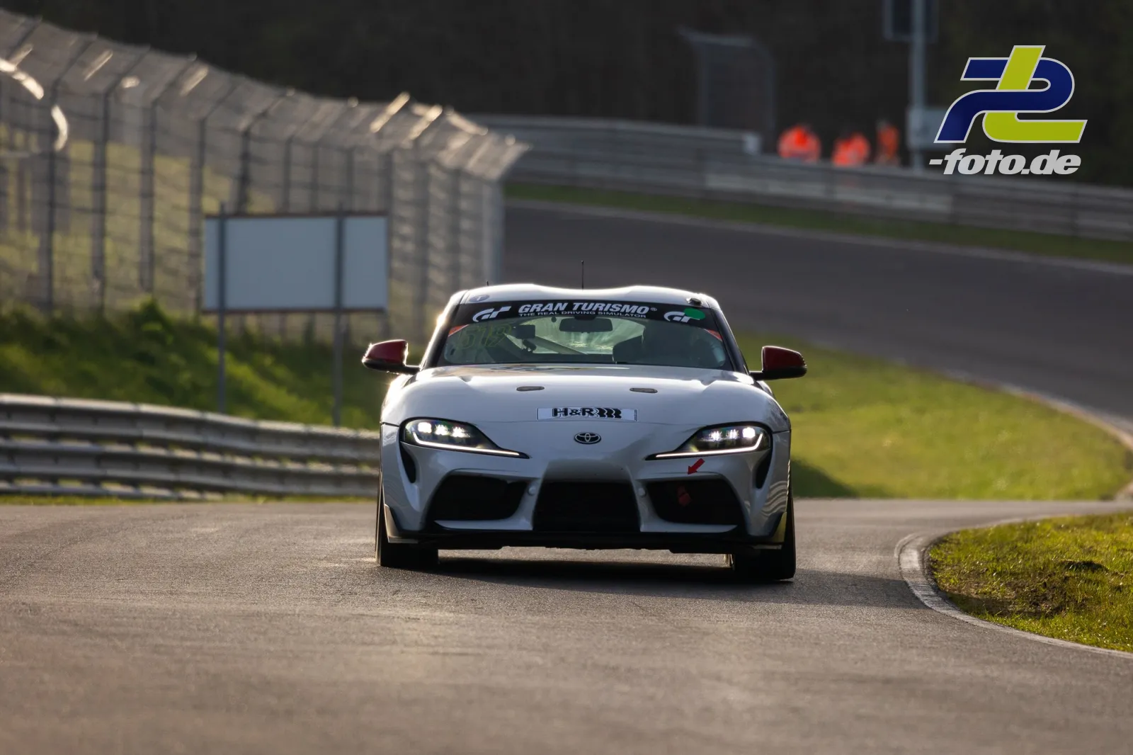 Weißer Toyota Supra mit H&R-Banderole im Zeittraining auf dem Nürburgring, Frontansicht in Kurvenausgang.