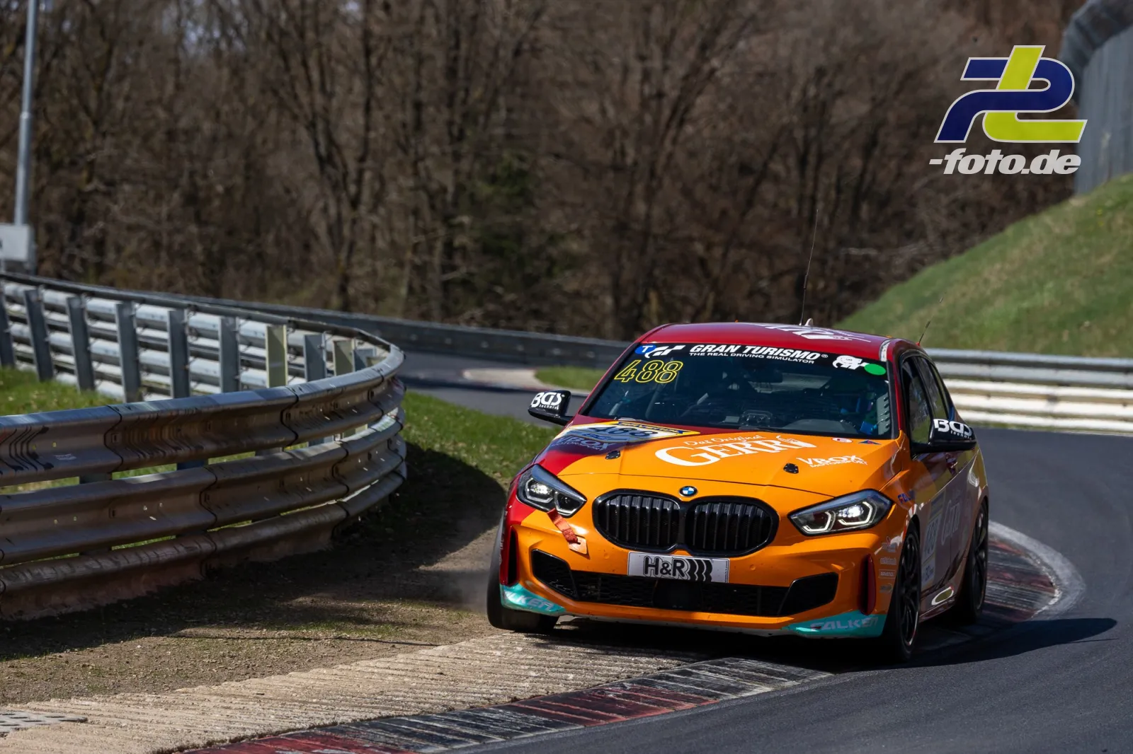 BMW Startnummer 488 in orange-roter Lackierung in einer Kurve der Nürburgring-Nordschleife während des NLS-Laufs.