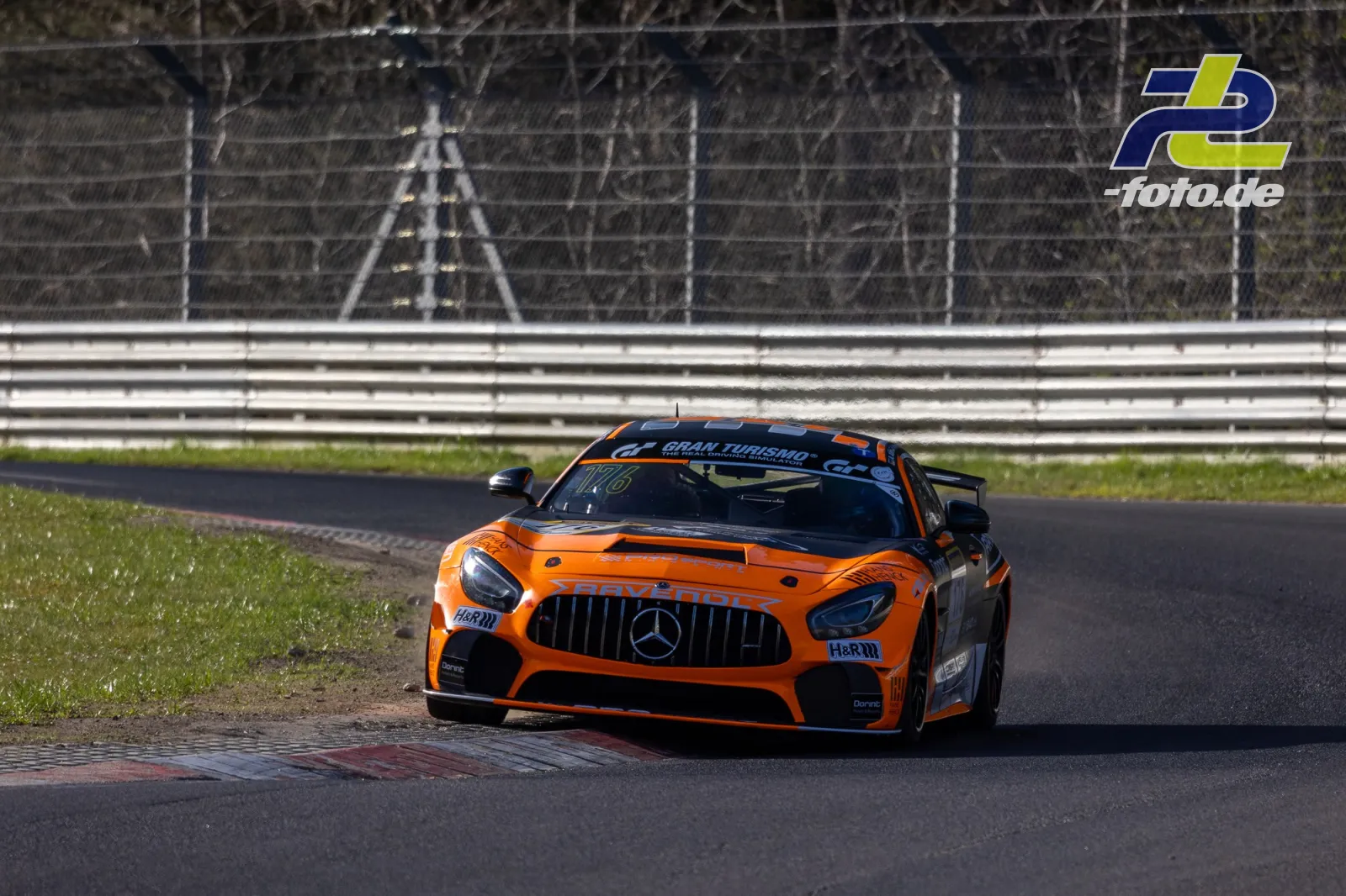 Oranger Mercedes-AMG GT3 mit schwarzen Akzenten in der Kurve am Nürburgring während des Zeittrainings, Randstein im Vordergrund.