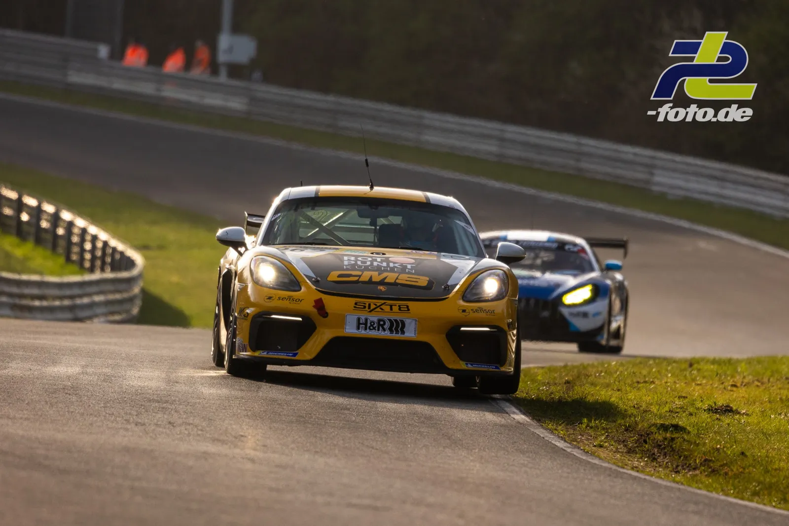 Porsche Cayman GT4 in gelb-schwarzer Lackierung vor einem Konkurrenten im Zeittraining beim Anbremsen einer Kurve.