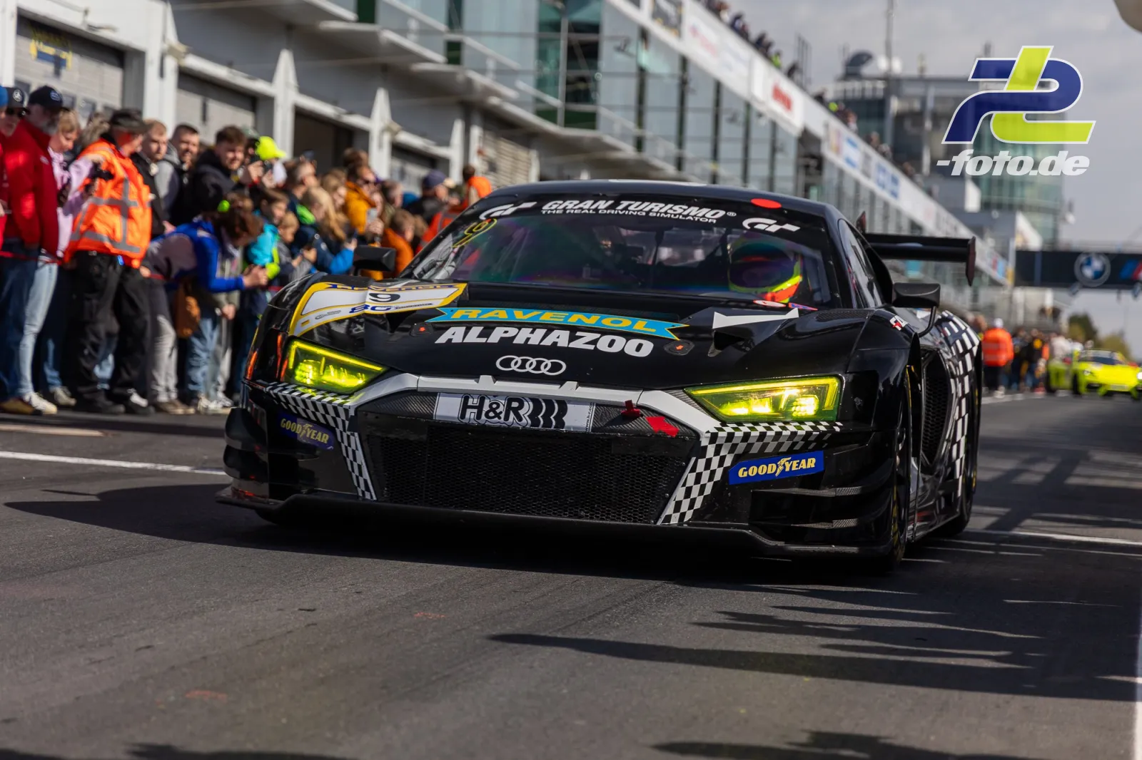Audi R8 LMS GT4 fährt auf der Nürburgring-Boxengasse an Zuschauern vorbei, Frontalansicht mit auffälligen gelben Scheinwerfern