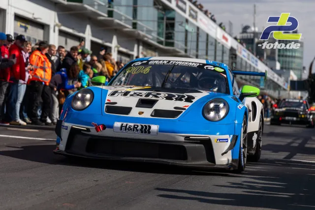 Porsche 911 GT3 Cup in blau-weißer H&R-Lackierung fährt auf der Boxengasse am Nürburgring vorbei an Zuschauern.